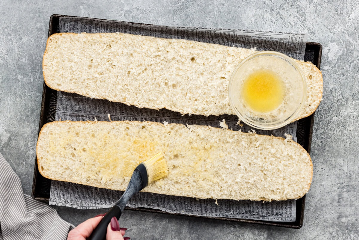 Basting garlic butter on halves of French bread