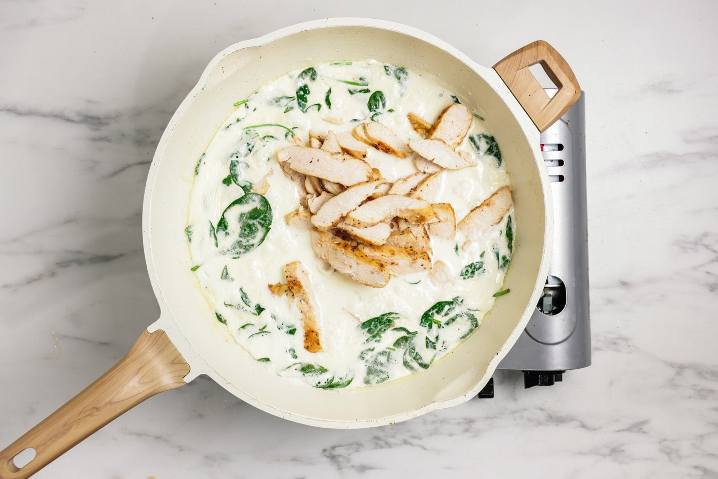 spinach and sliced chicken added to garlic cream sauce in a skillet