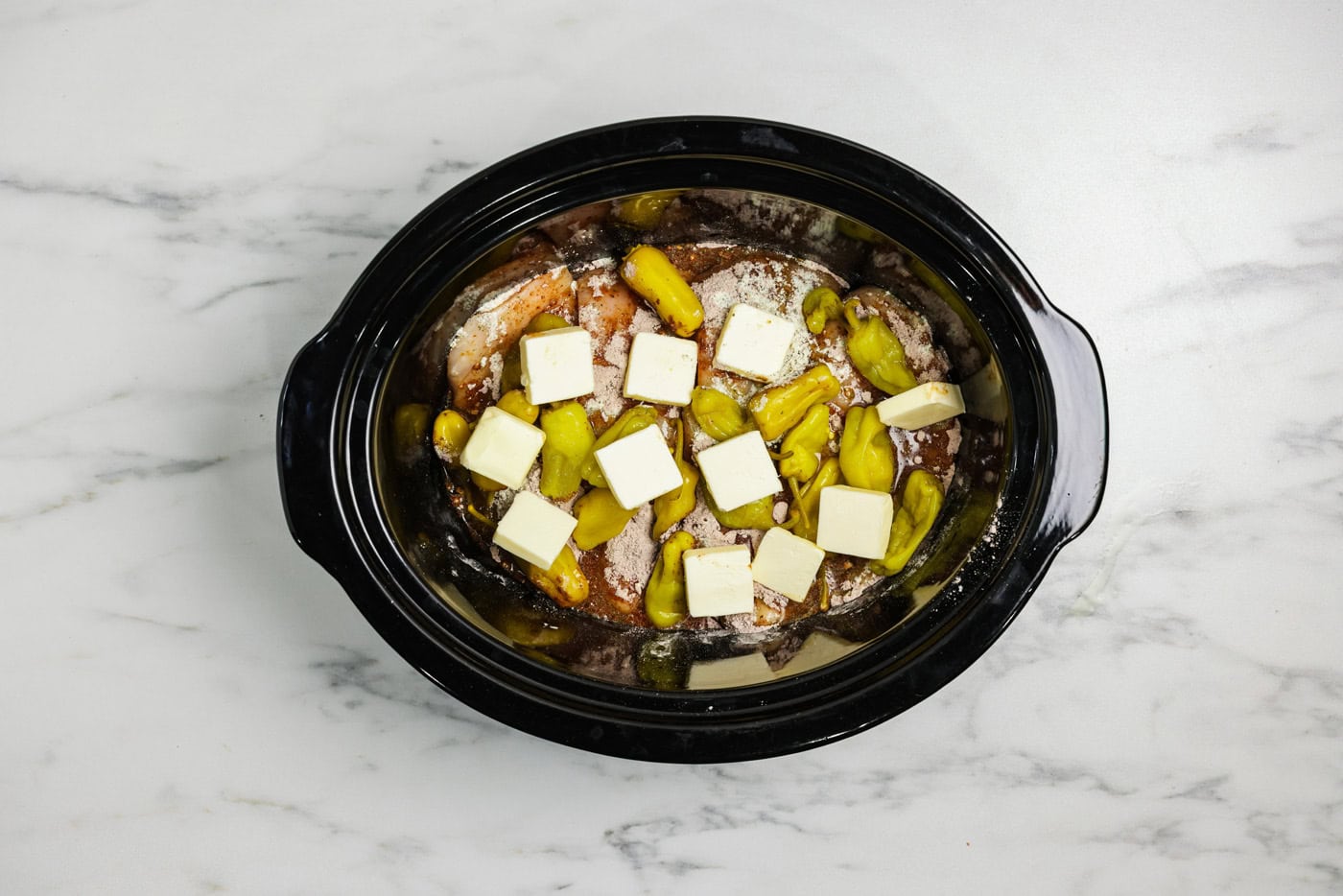 Butter pats on top of pepperoncinis, ranch seasoning, Au jus packet, and chicken breasts in a crock pot