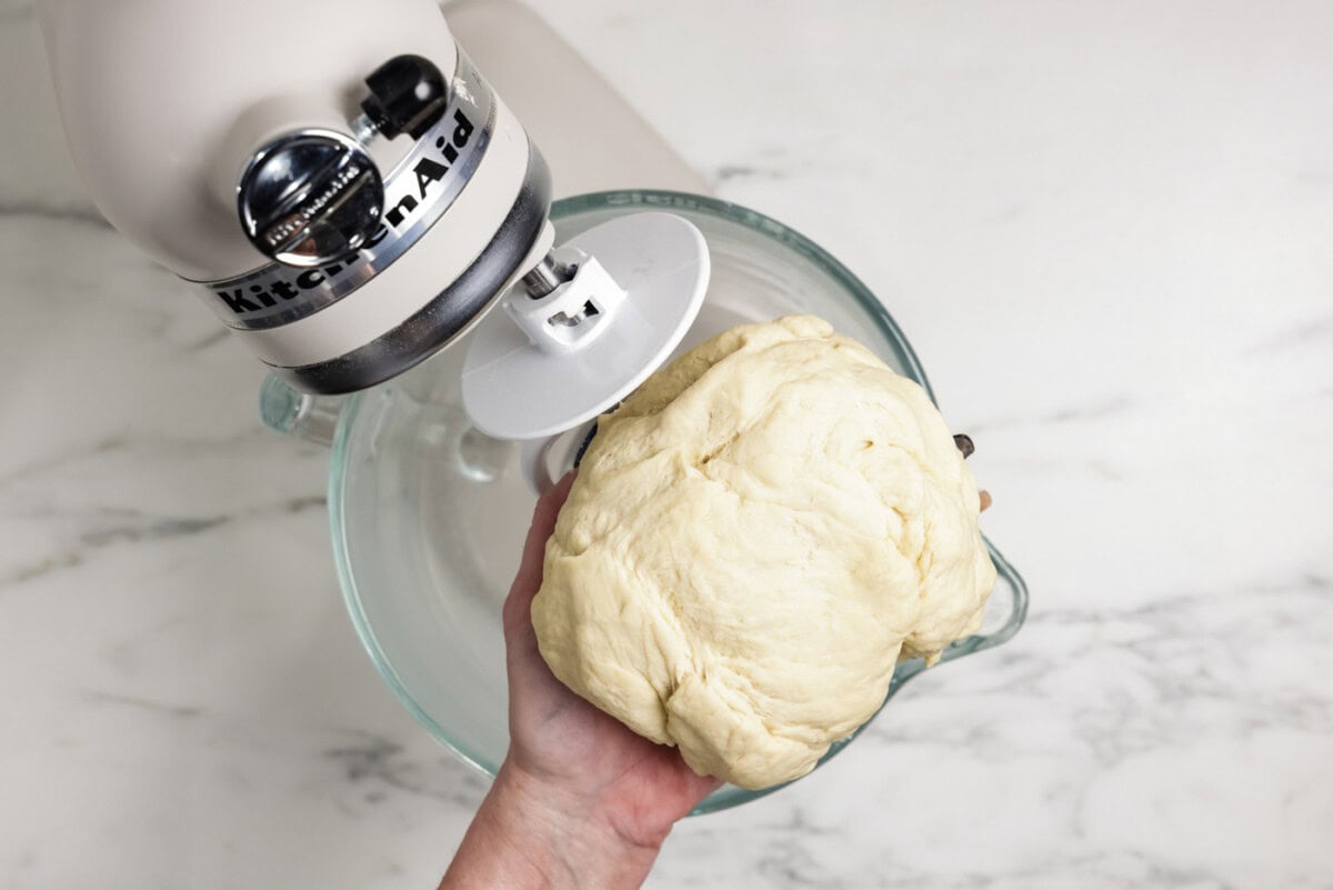 Hand holding bread dough over a stand mixer