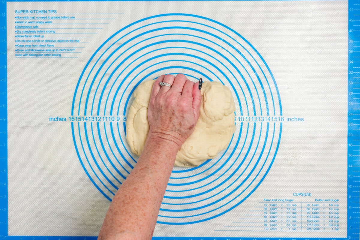 Hand pressing bread dough onto a floured surface