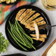 Plate of Parmesan Crusted Chicken cut into slices with green beans on the side