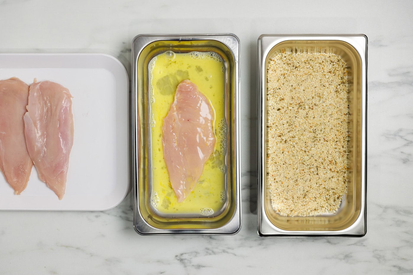 chicken breast in a breading tray with egg and water