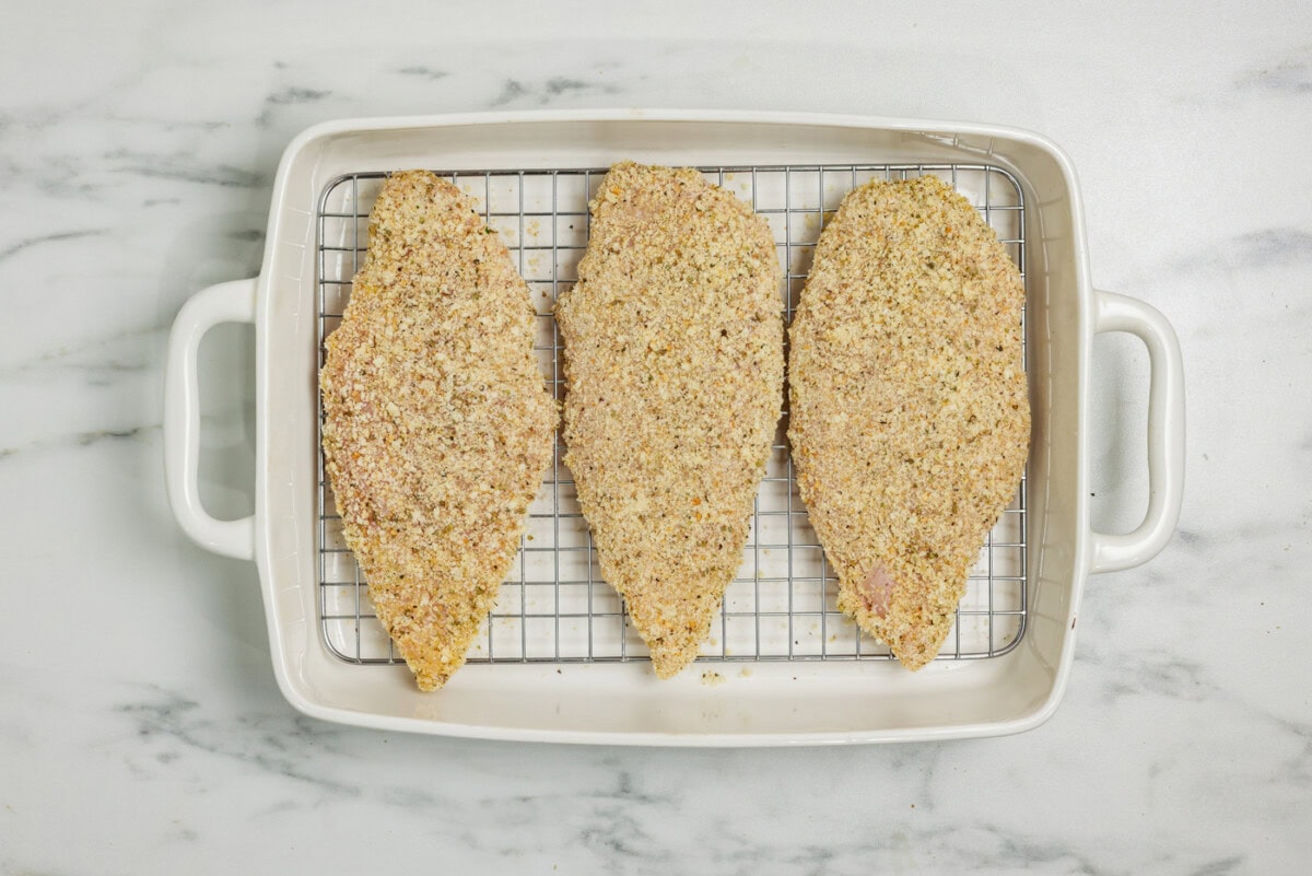 parmesan and breadcrumb coated chicken breast in a baking pan lined with a wire rack
