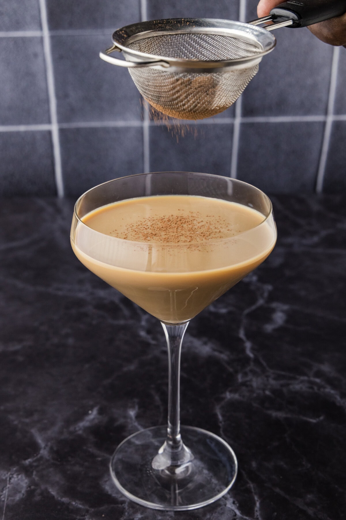 Dusting cocoa powder over Baileys chocolate martini with a small sieve