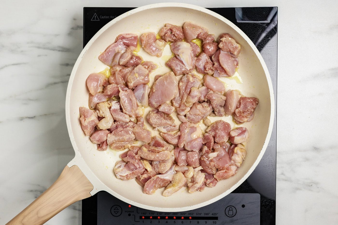 Cubes of chicken coated in flour cooking in a skillet with oil