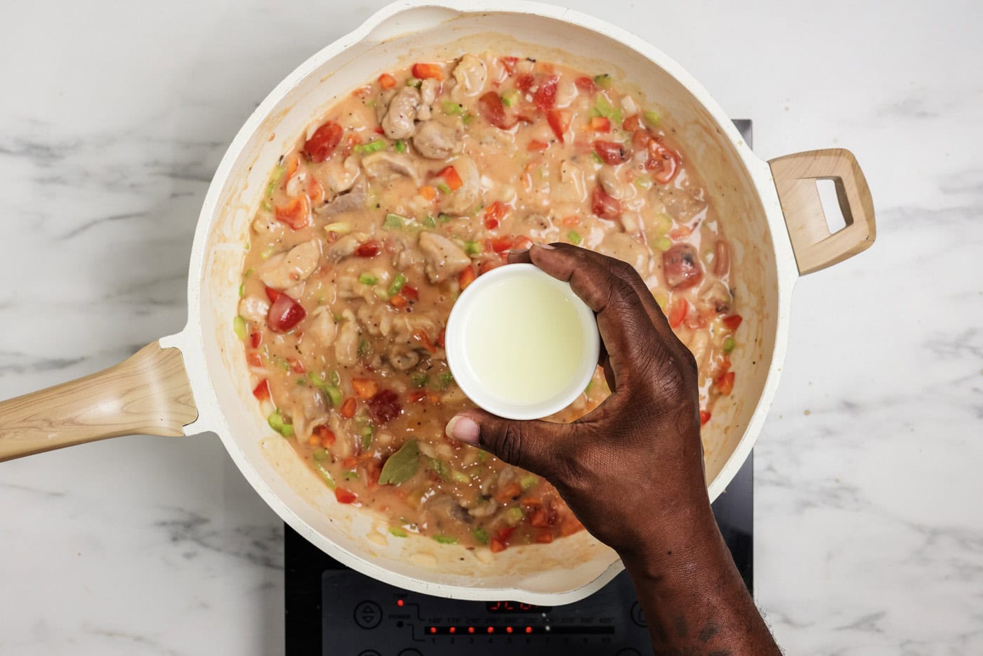 Hand holding small bowl of lemon juice over a skillet of chicken etouffee
