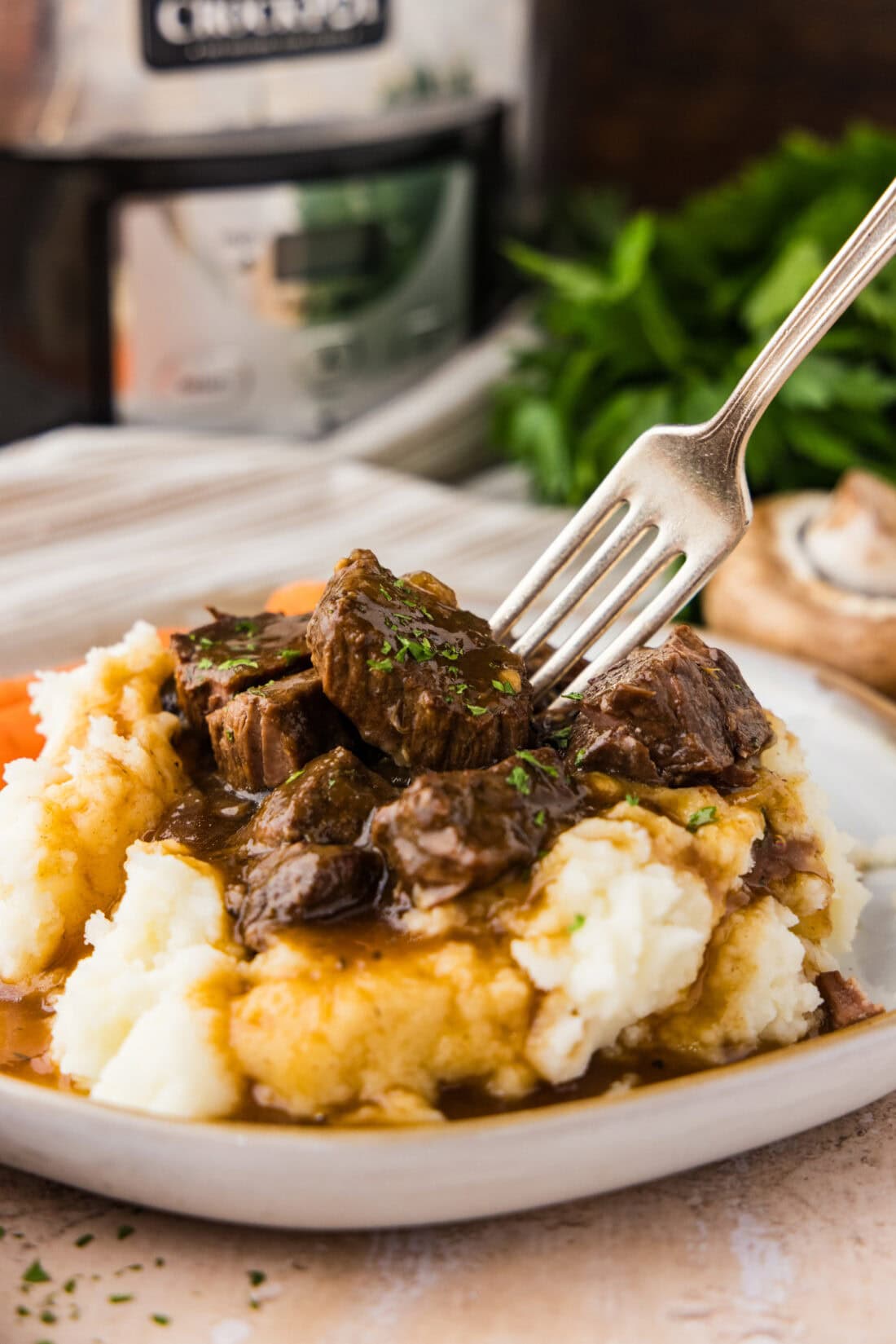Fork pressing into Crockpot Beef Tips and Gravy served over mashed potatoes