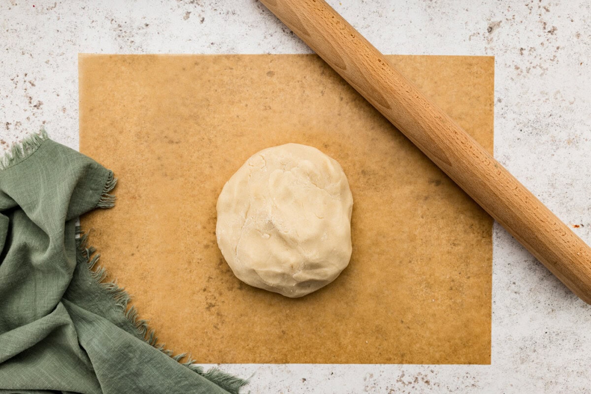 Shortbread dough ball on parchment paper next to a rolling pin