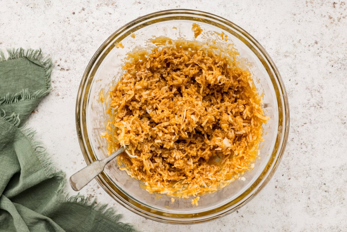 Toasted coconut mixed with melted caramel in a bowl with a spoon