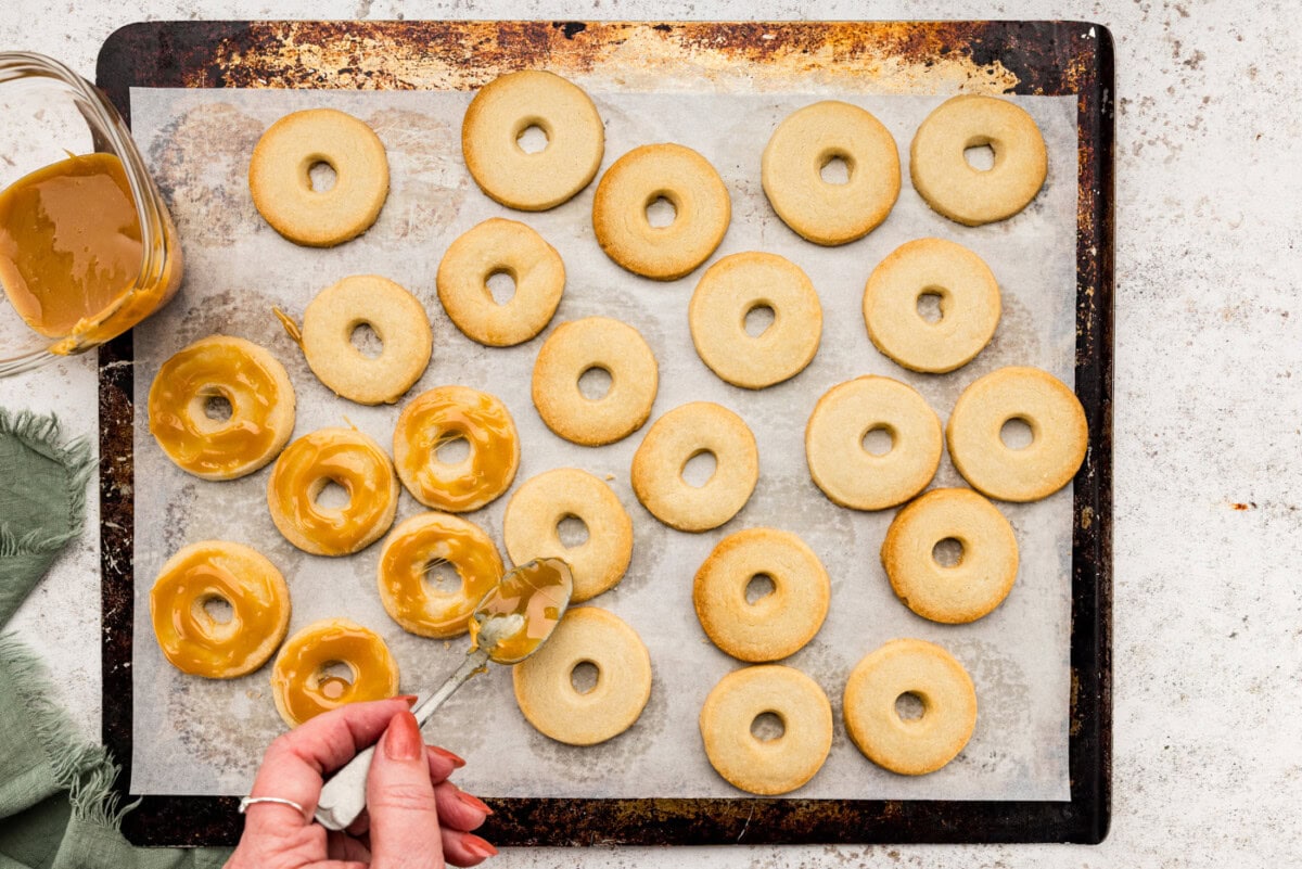Using a spoon to spread caramel over shortbread cookie circles