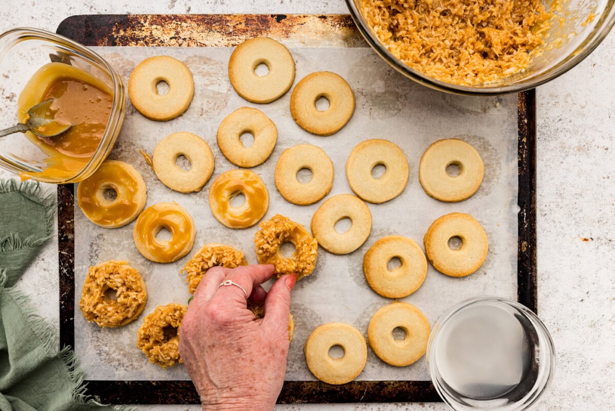 Hand spreading caramel coconut topping over cookie rounds