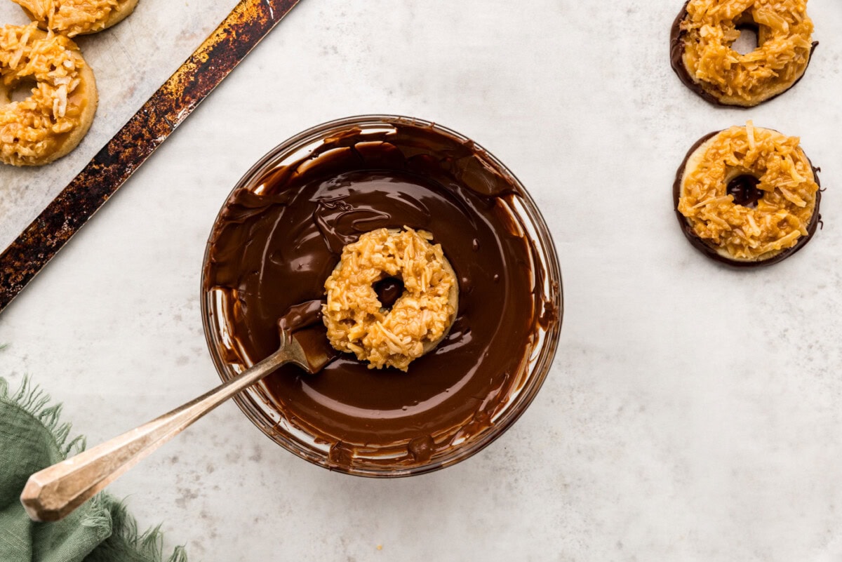 Fork dipping caramel coconut cookies into chocolate