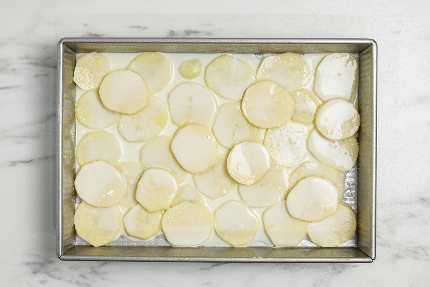 Broth sauce mixture on top of sliced potato rounds in a baking pan