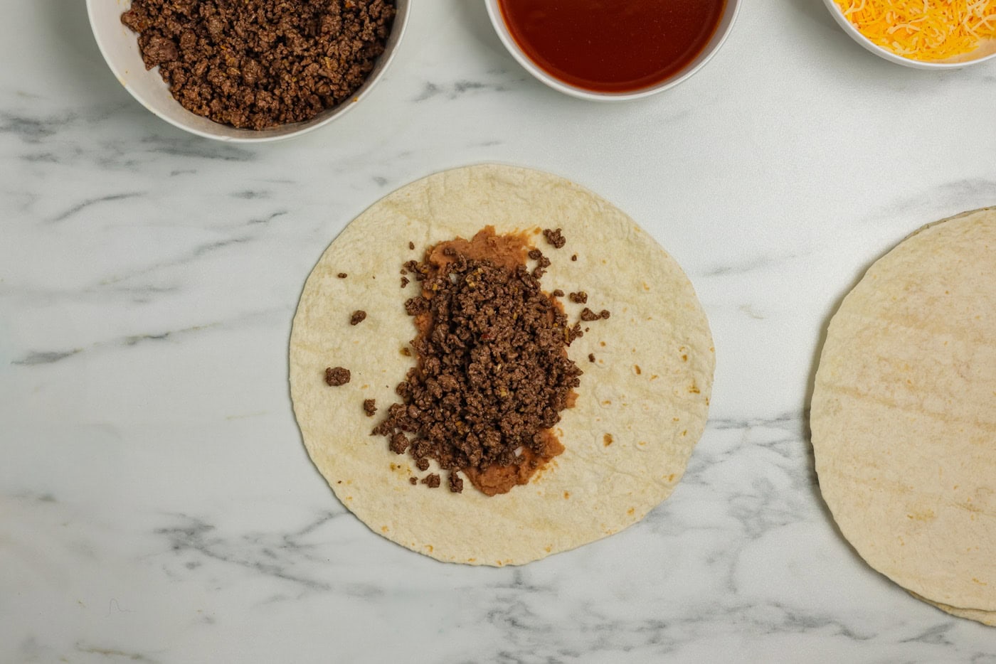 ground beef overtop refried beans and diced onion on a tortilla