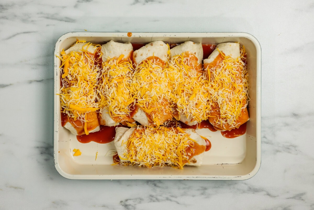 enchiritos in a baking pan topped with enchilada sauce and cheddar cheese