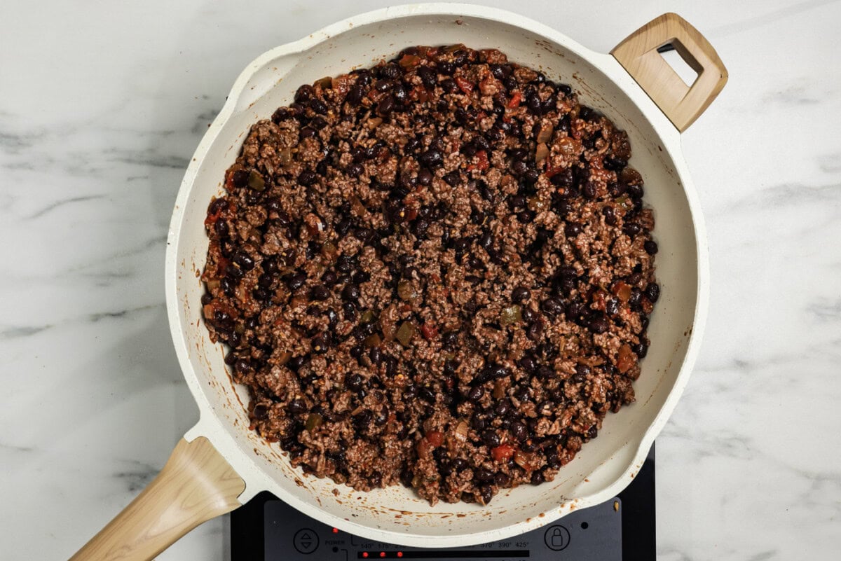 Cooked ground beef with black beans, seasoning, and salsa mixed together in a skillet