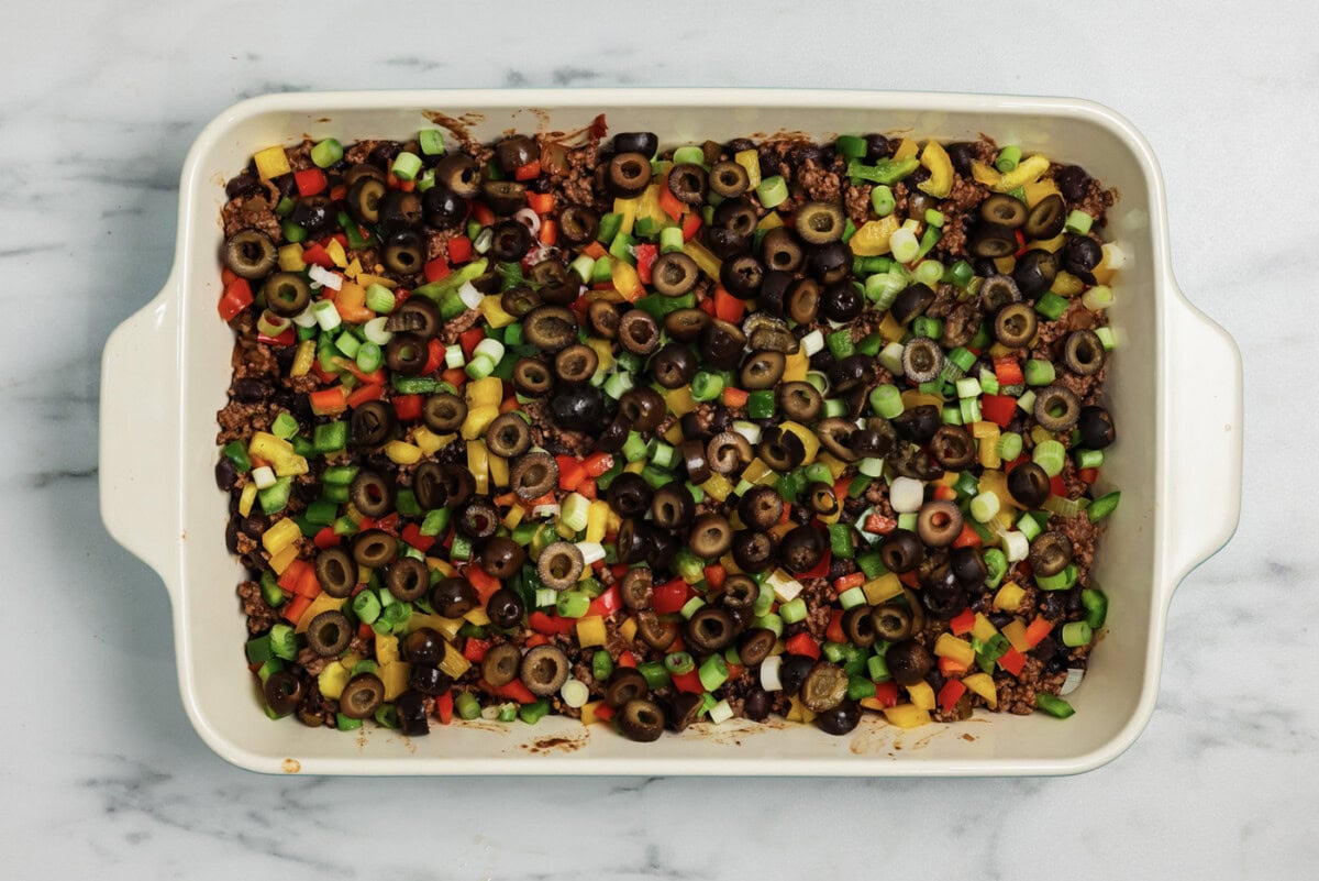 Black olives on top of ground beef mixture and fresh chopped vegetables