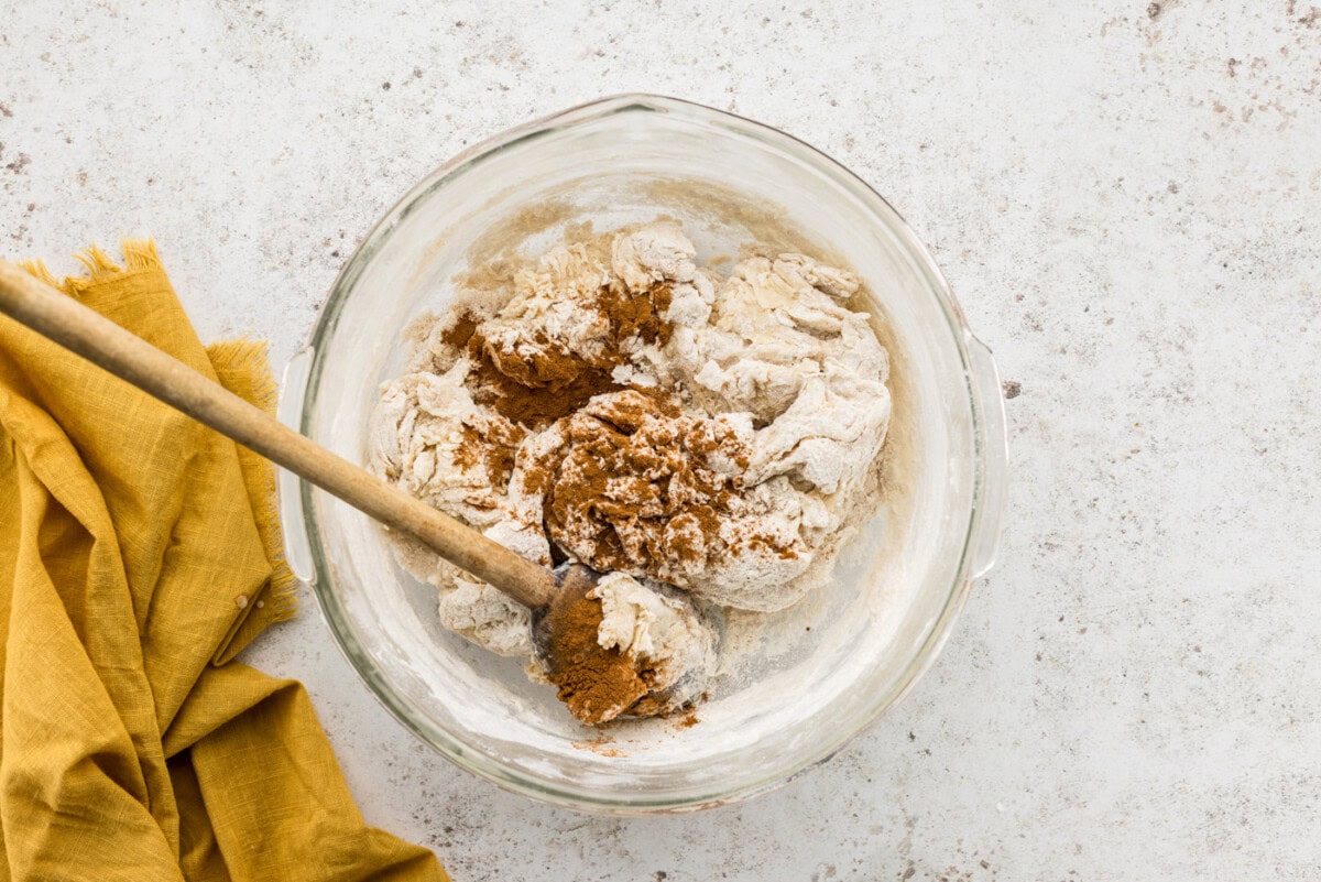 Wooden spoon stirring cinnamon into bowl of concha dough
