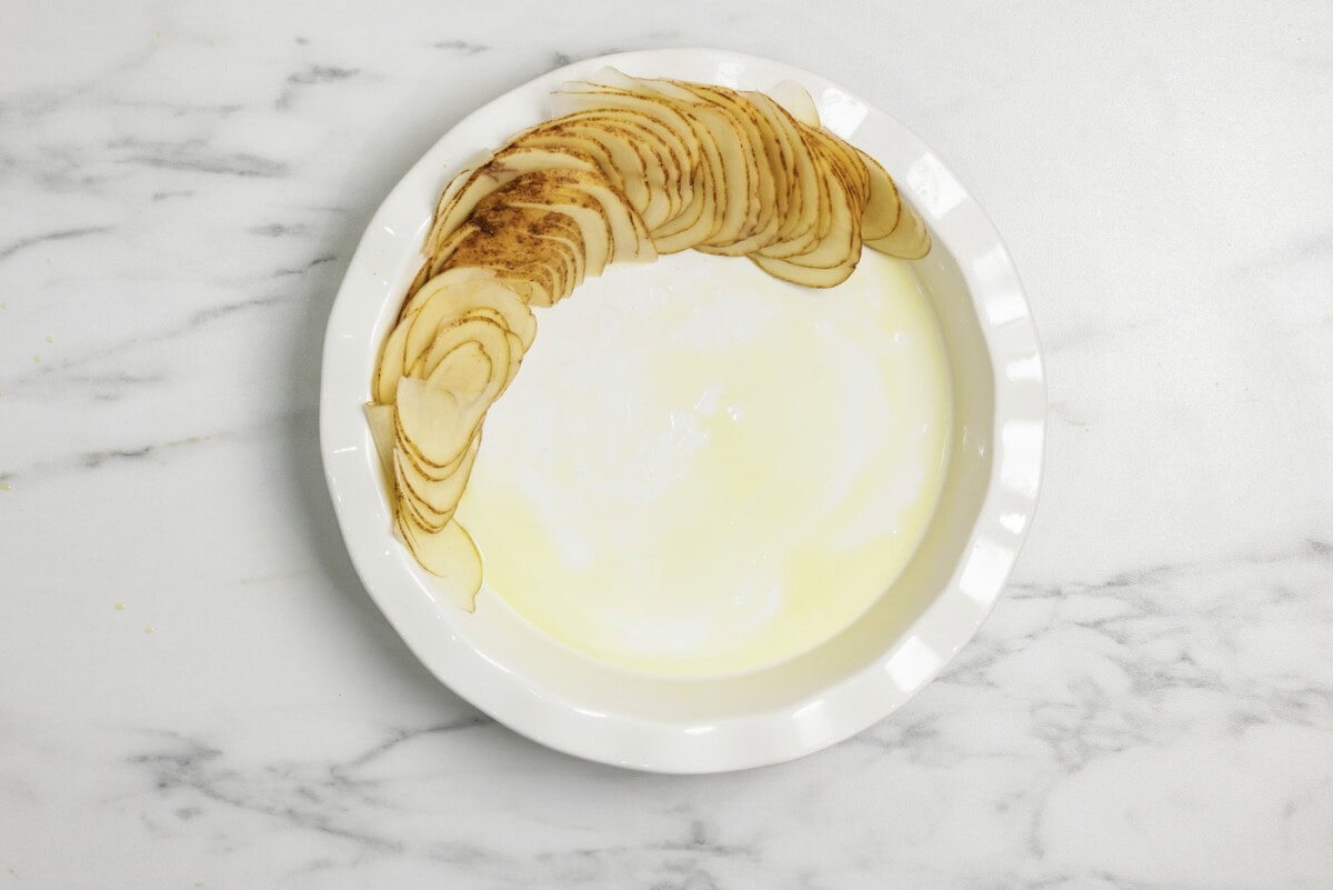 Sliced potatoes stacked along the edge of a deep dish pie plate