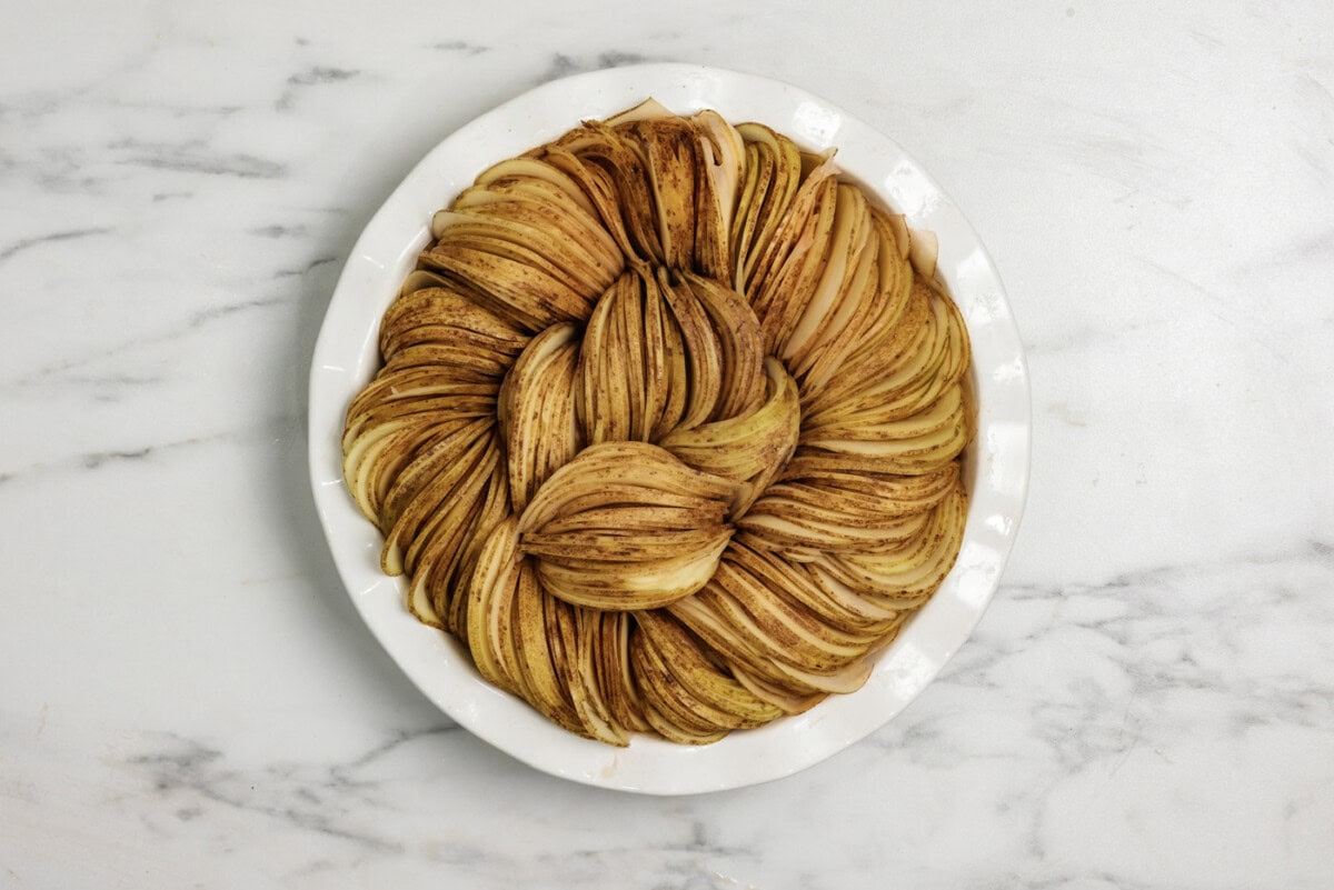 Sliced potato rounds stacked inside a deep dish pie plate in a circle