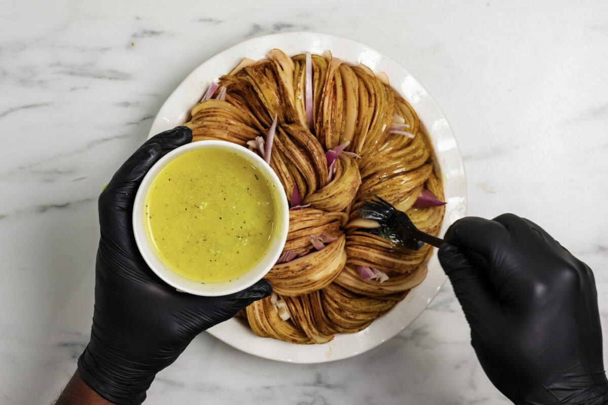Brushing the top of sliced crispy roast potatoes with melted butter mixture
