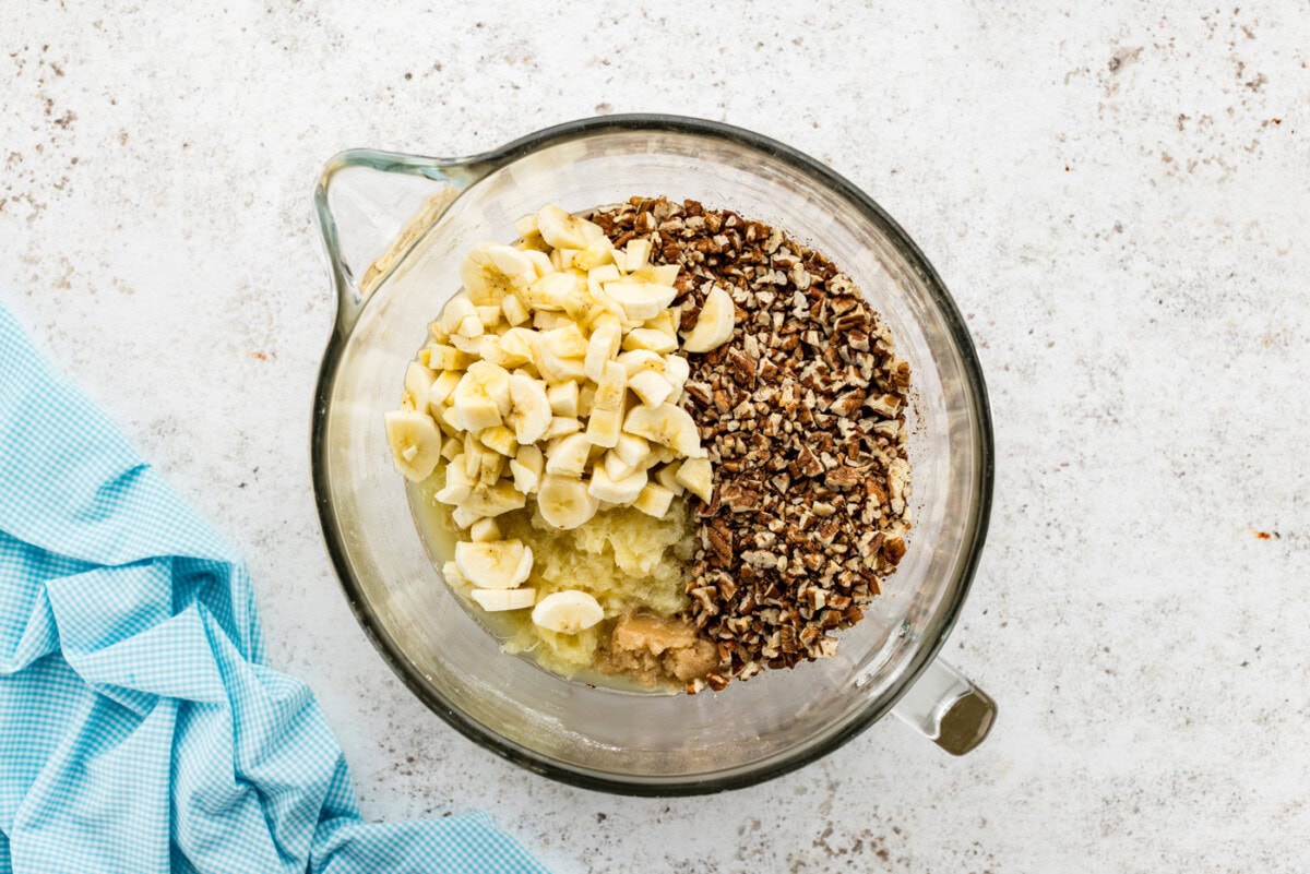 Chopped pecans, crushed pineapple, and bananas added to cake batter in a bowl