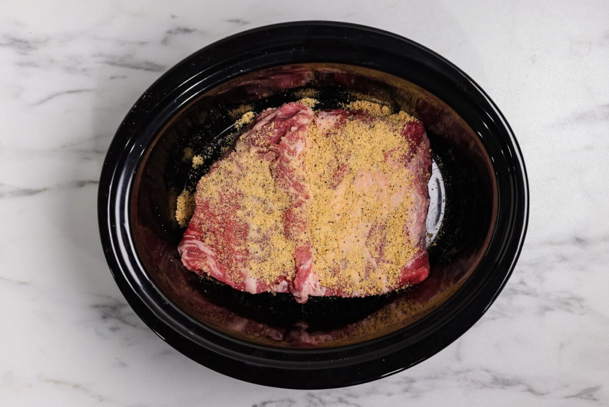 spice mixture on top of raw brisket in crockpot