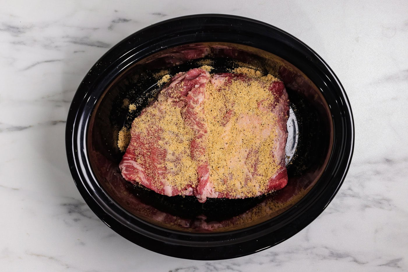 spice mixture on top of raw brisket in crockpot