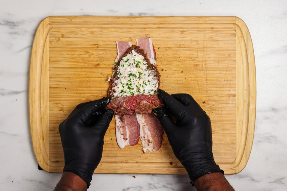 hand rolling up cube steaks with cream cheese on top of bacon