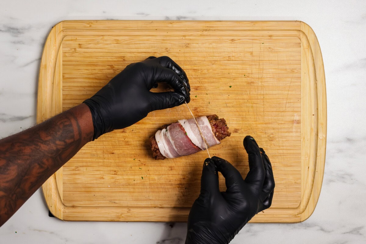 hand tying twine over bacon wrapped cube steaks