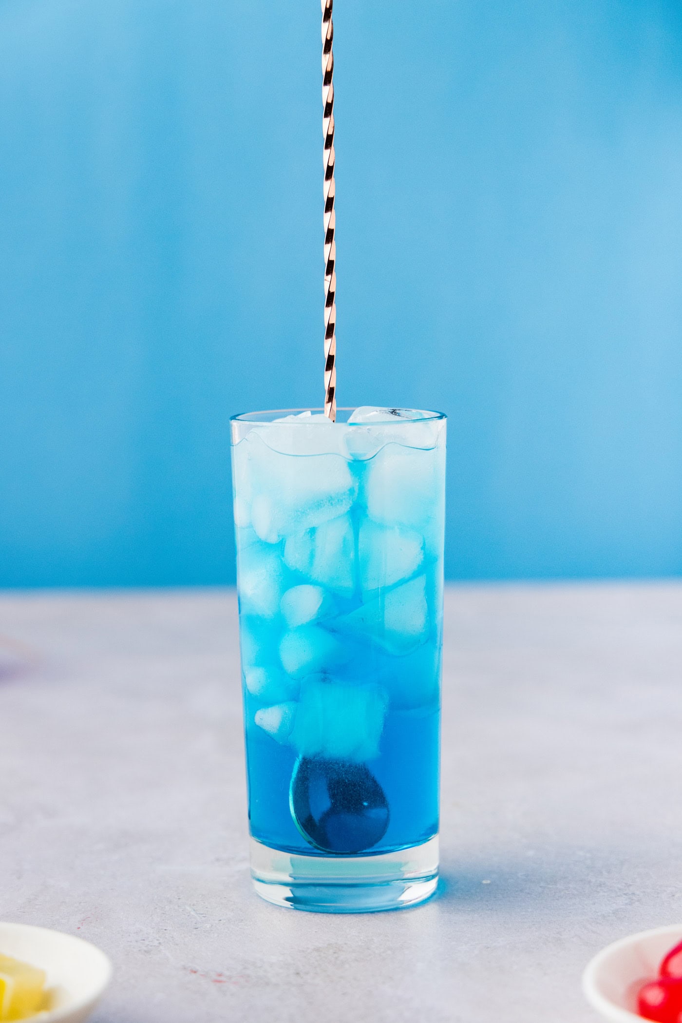 glass of Blue Mermaid Cocktail with a spoon stirring it