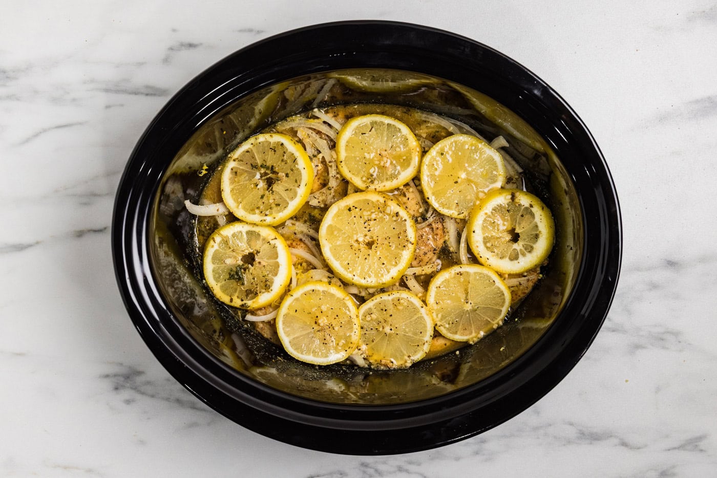 chicken in crockpot covered in lemons with drippings