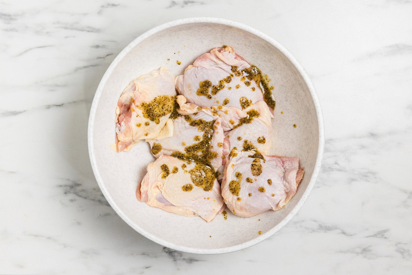 seasoning and oil mixture drizzled on to raw chicken thighs