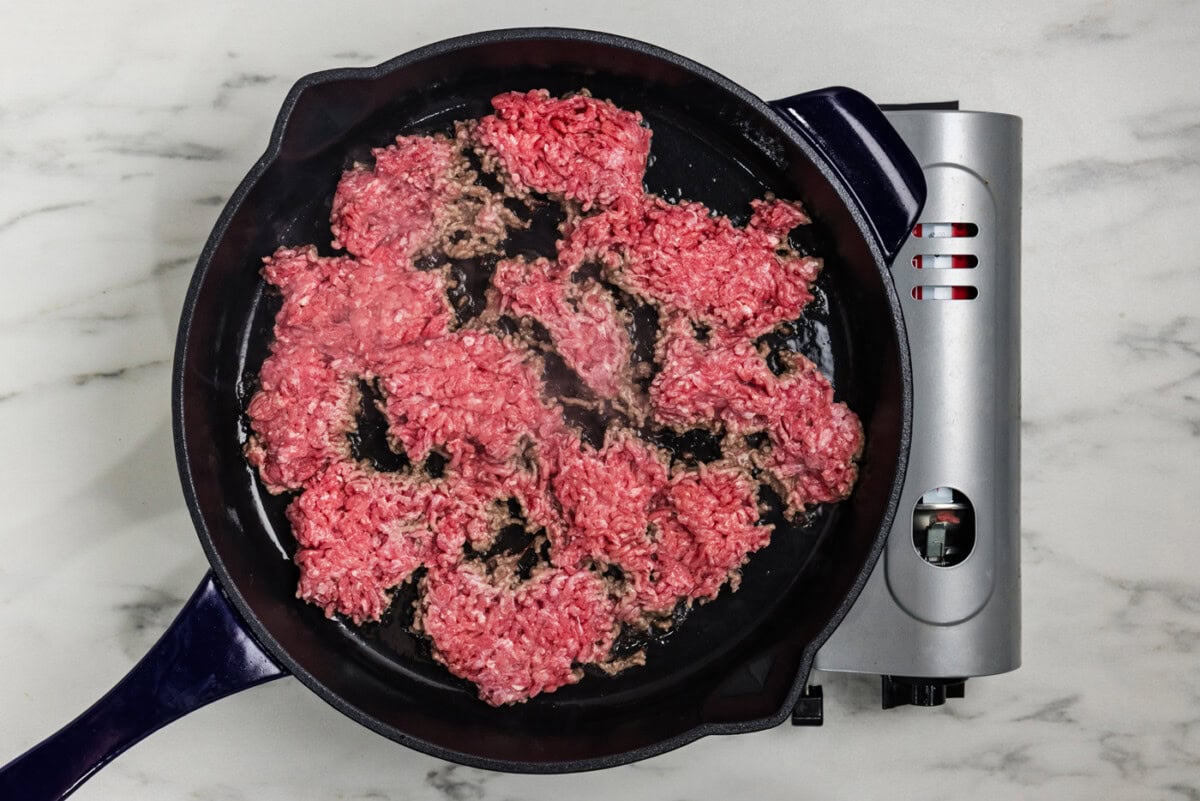 chunks of ground beef sizzling and developing a crust in a hot skillet