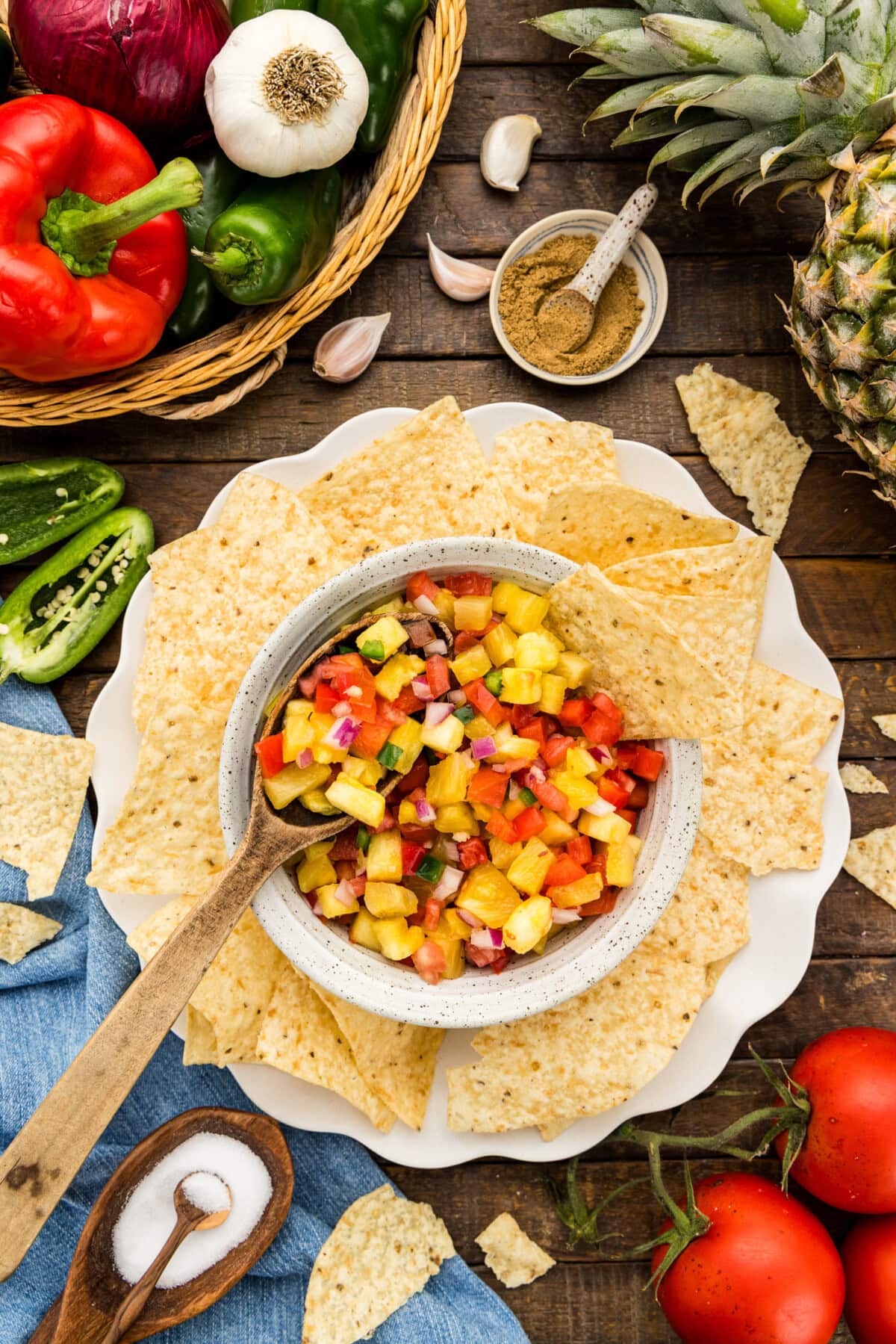 bowl of Pineapple Salsa with spoon surrounded by peppers, tomatoes, pineapple