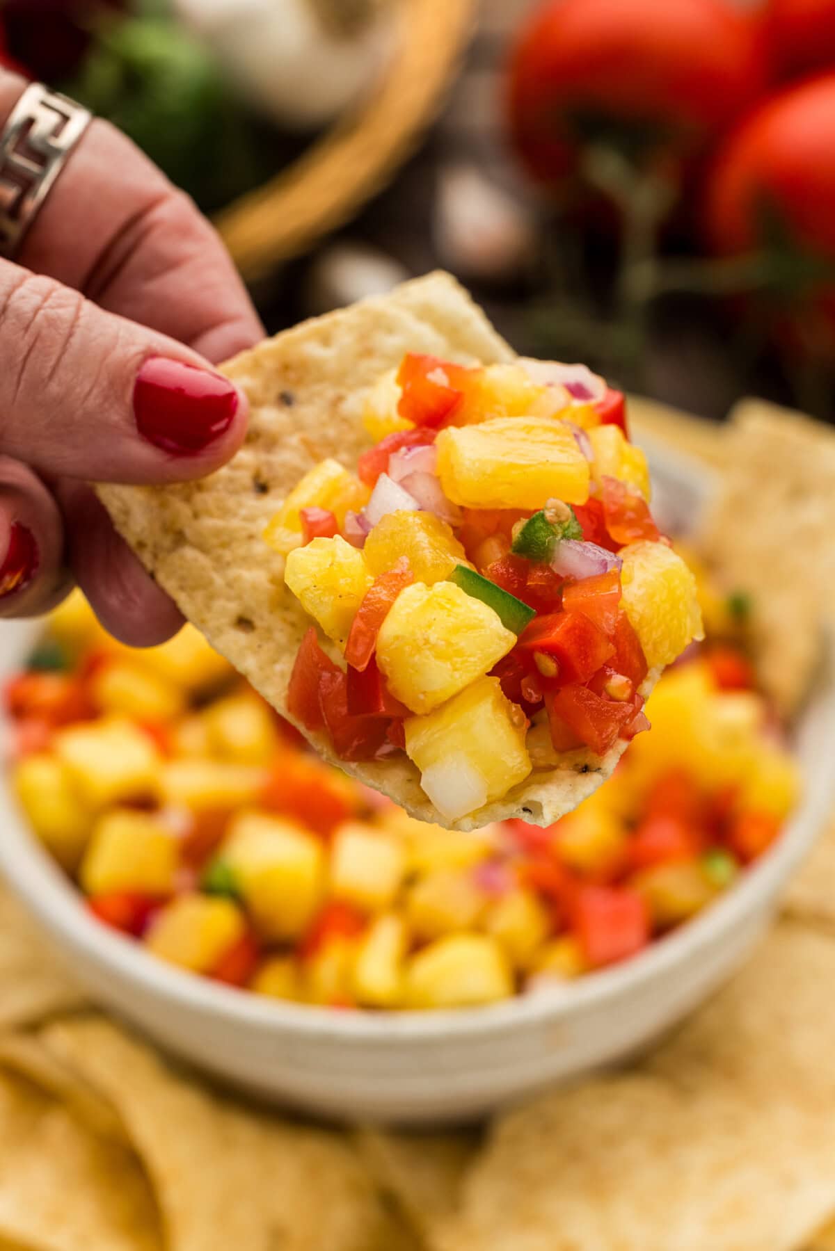 hand lifting a chip with Pineapple Salsa