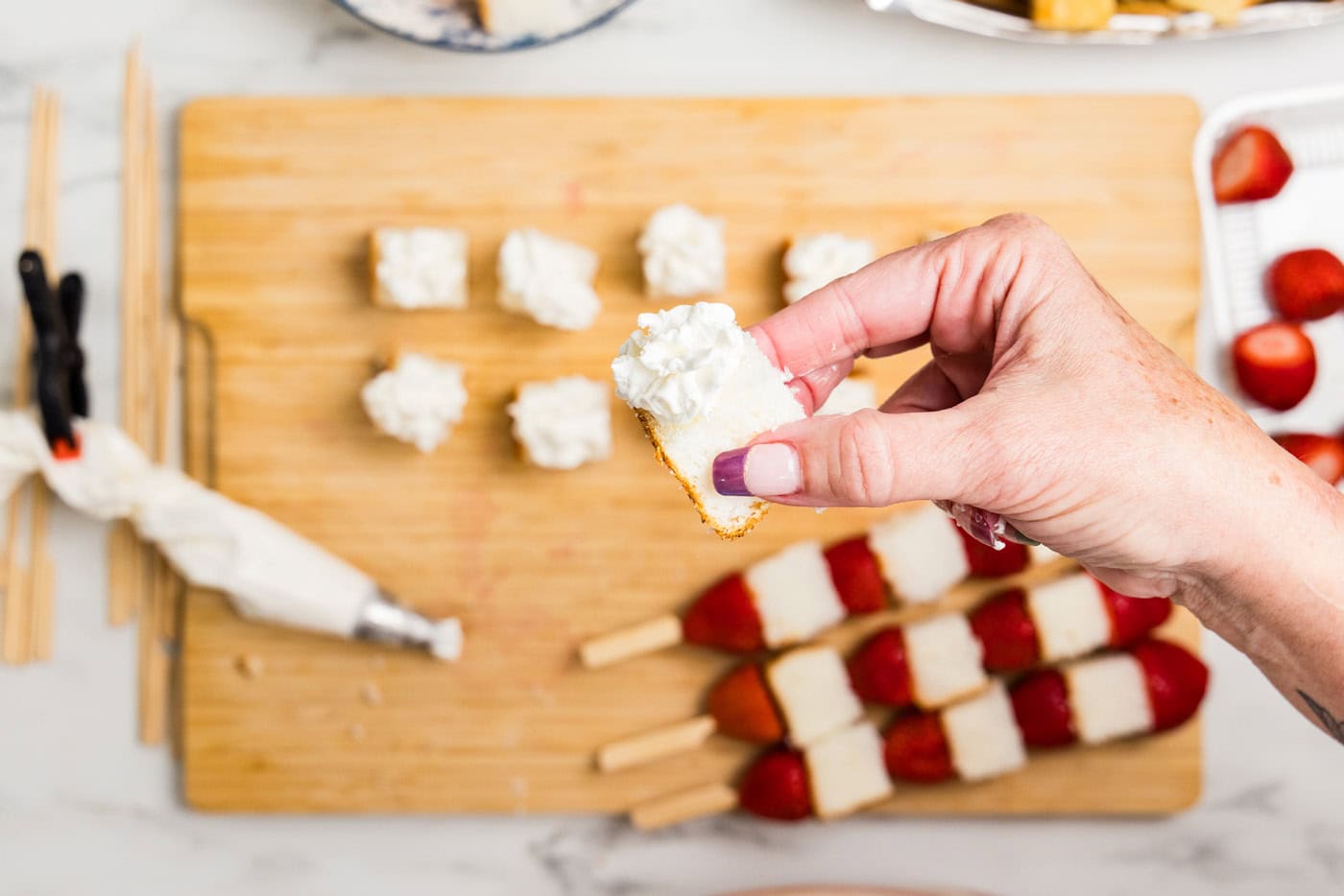 hand holding cubed angel food cake with whipped cream on it