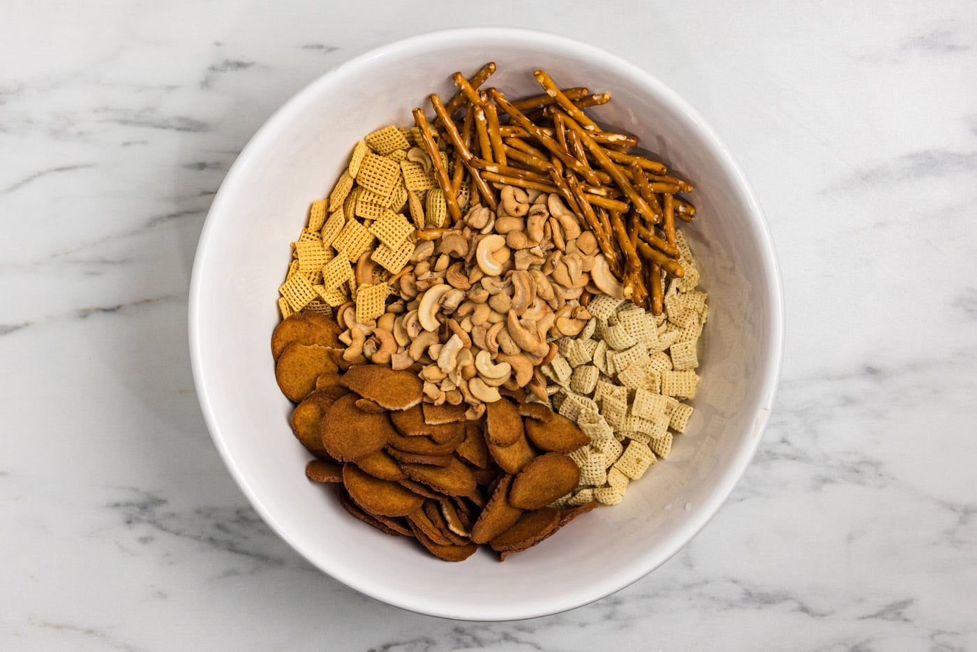 cereals, rye chips, pretzel sticks, and cashews in a mixing bowl