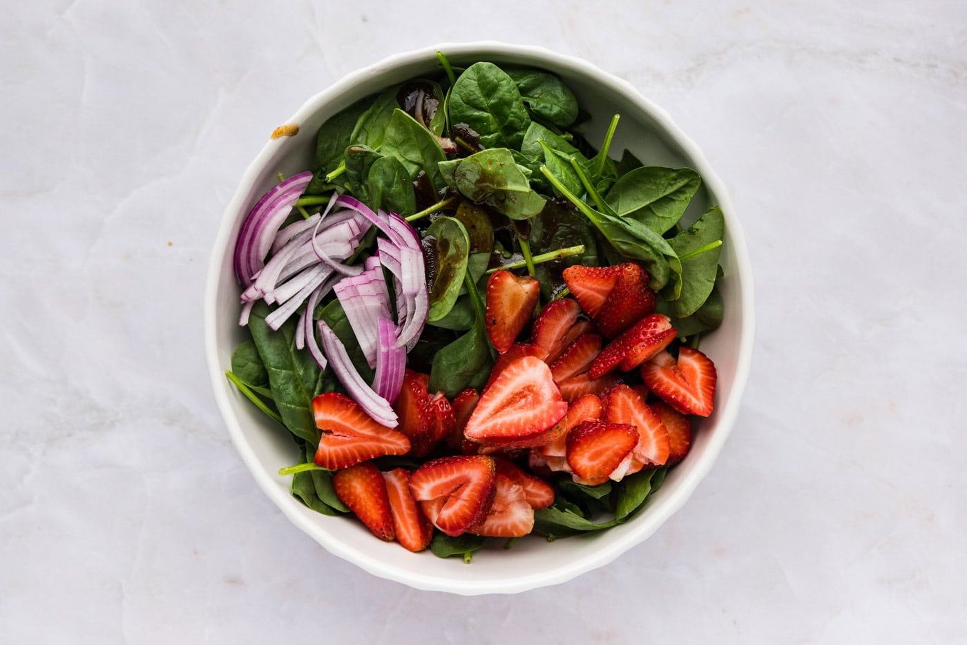 Strawberries, spinach, and red onion in a bowl with dressing