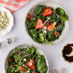 two small bowls of Strawberry Spinach Salad with extra ingredients near it
