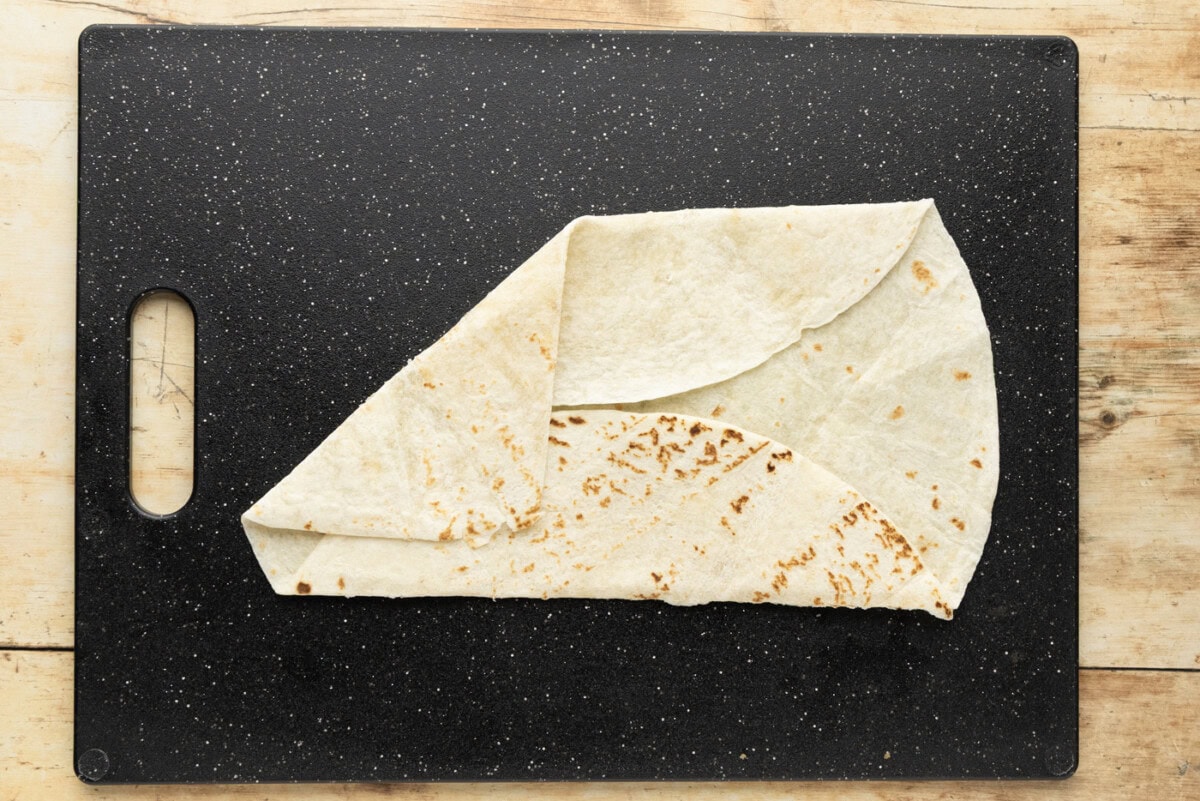 Crunchwrap fold in progress with the first diagonal section brought up over the center and overlapping the flat fold above it