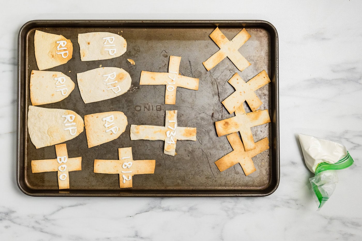 Toasted tortilla tombstones and crosses lettered with RIP and BOO in sour cream beside a snipped piping bag