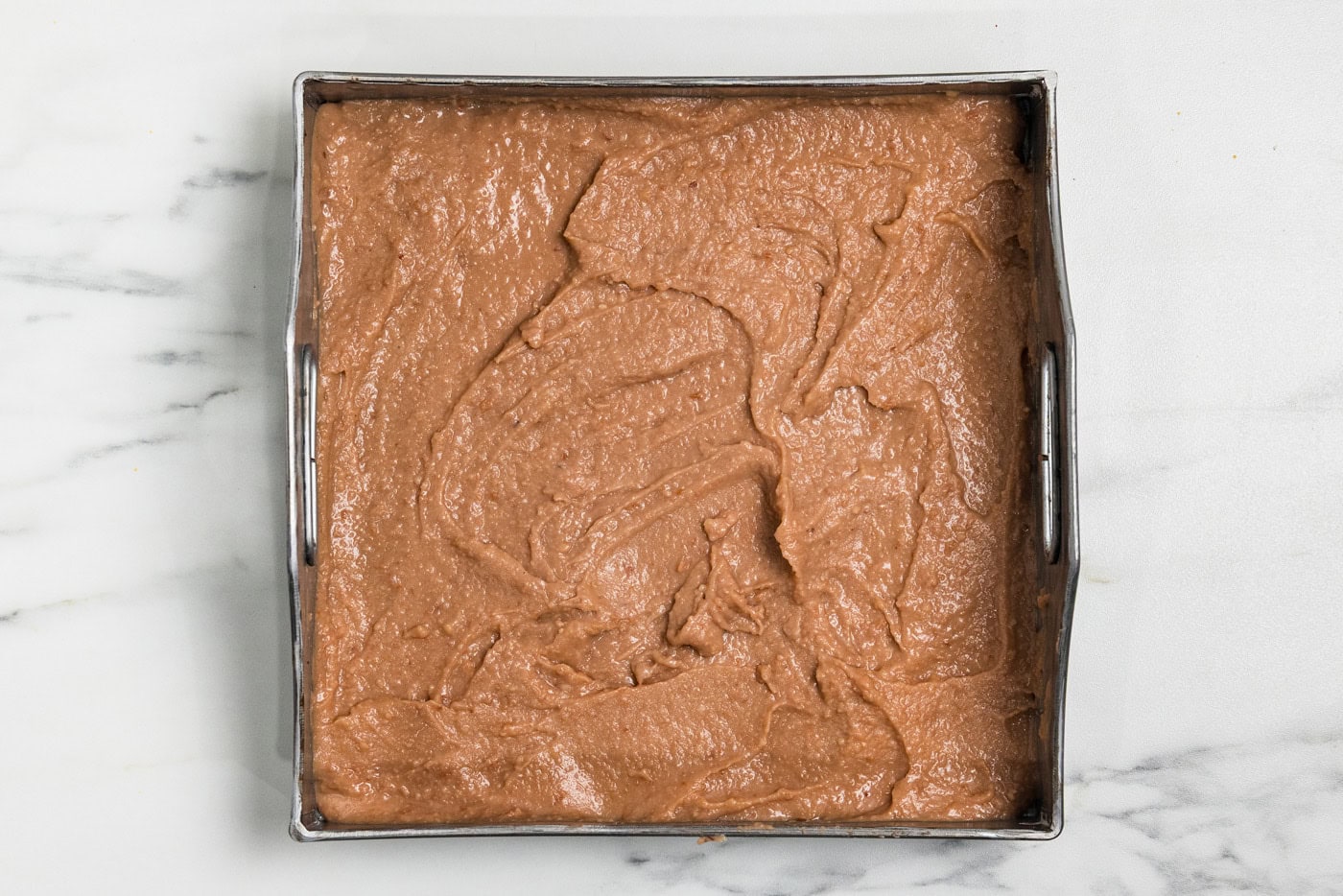 Refried beans spread in an even layer in the bottom of a square baking pan