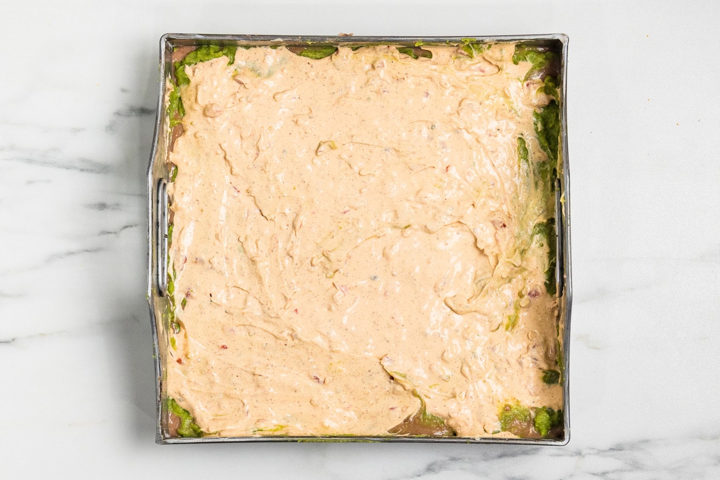 Seasoned cream cheese mixture spread over the guacamole layer in a square baking pan