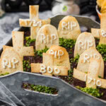 Graveyard taco dip topped with tortilla tombstones and chive grass, styled with cobwebs and a skeleton hand