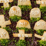 Graveyard taco dip garnished with chive grass and lettered tortilla tombstones surrounded by cobwebs