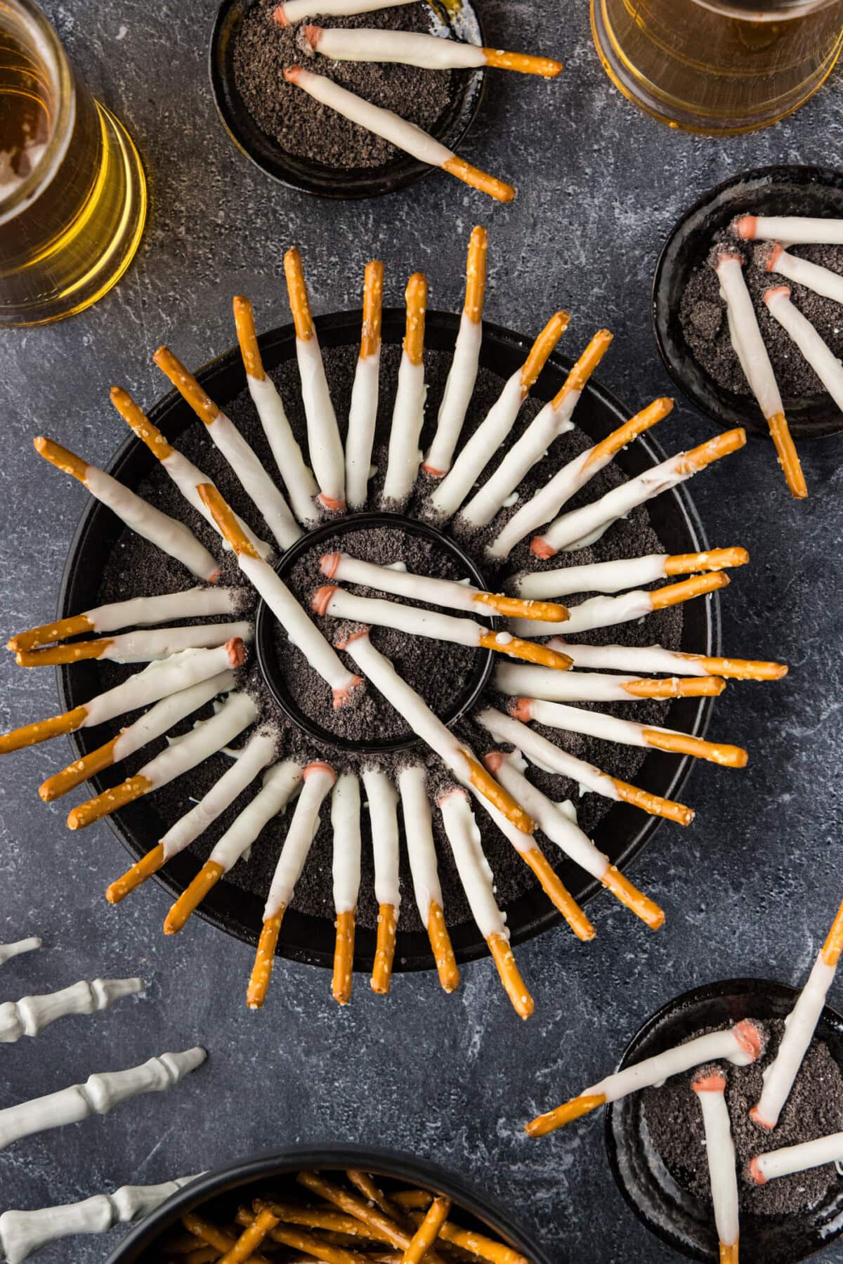 overhead view of Halloween Cigarette Pretzels on a table with drinks and a skeleton hand