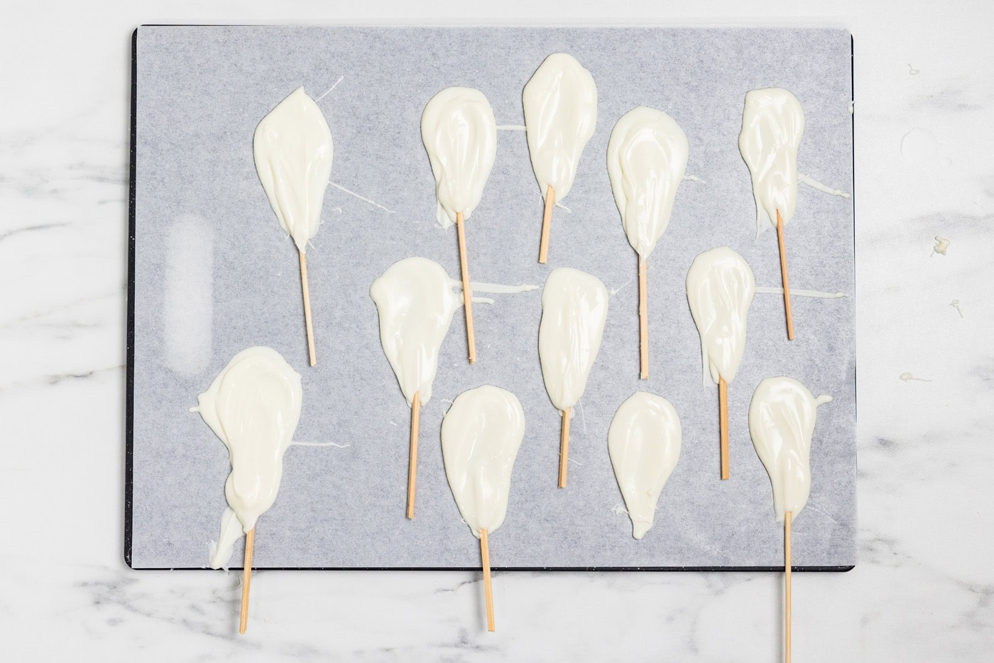 A tray of white chocolate ghost pops on lollipop sticks setting on wax paper
