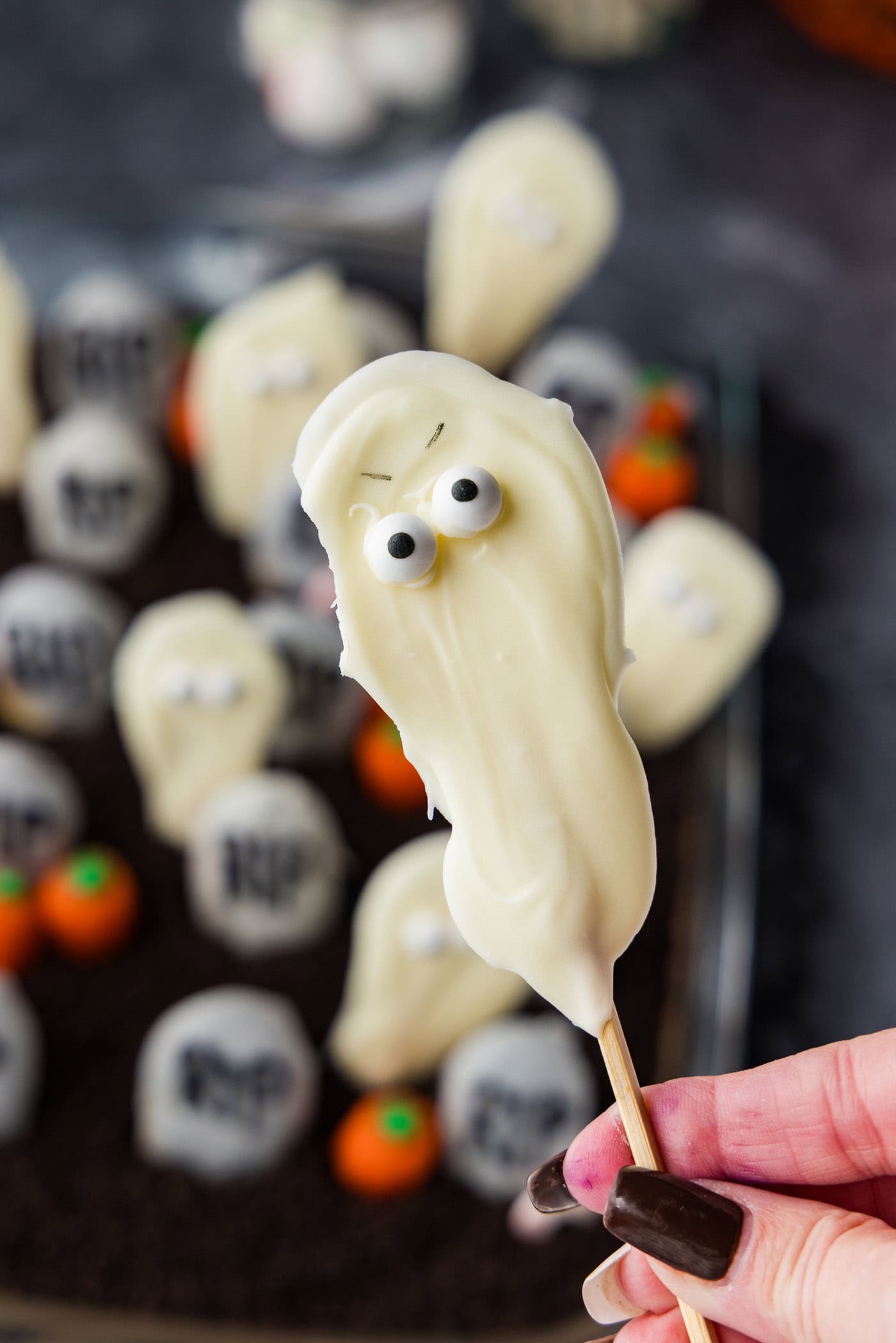 A white chocolate ghost pop held up over the finished Halloween dirt cake